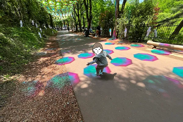 林の中にたくさん吊るされたカラフルな傘の回廊ではしゃぐ様子
