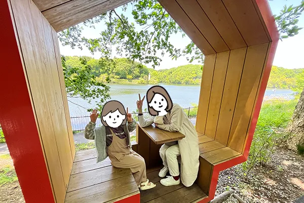 宮沢湖を背景に木製の家型をしたベンチに座って記念撮影する様子