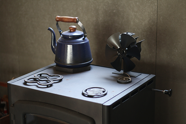薪ストーブの天板に栗原はるみのホーローケトルとストーブファンと五徳が置かれた様子